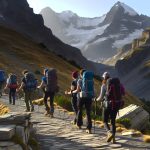 Un groupe de randonneurs marchant sur un sentier montagneux dans les Pyrénées, avec des sommets enneigés en arrière-plan.