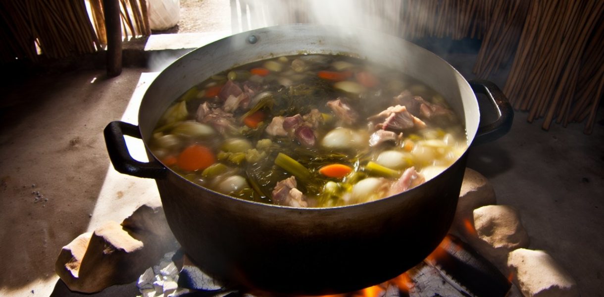 Un pot-au-feu traditionnel mijotant dans une marmite sur le feu, avec des légumes et de la viande visibles.